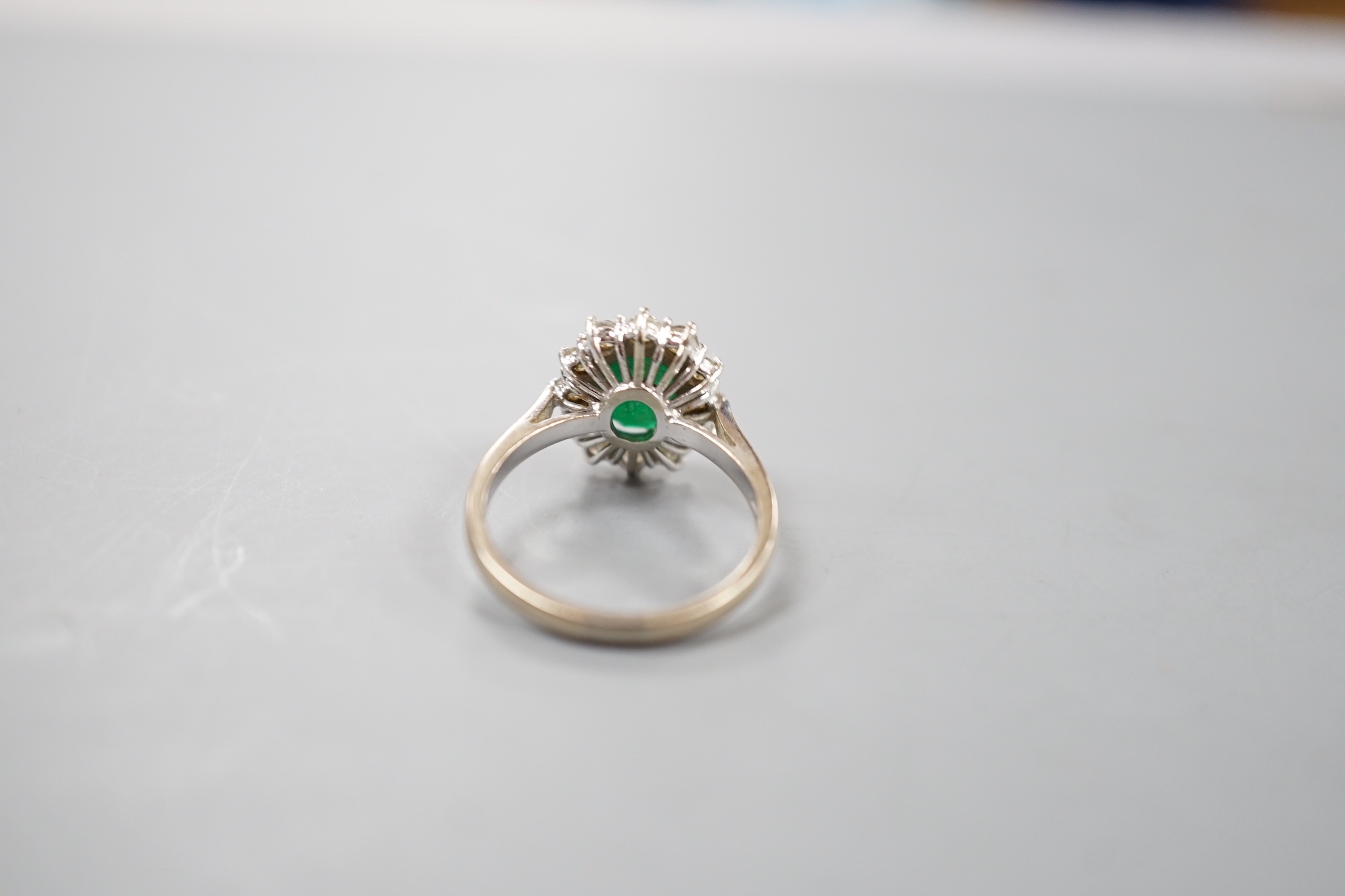 A modern 18ct white gold emerald and diamond set oval cluster ring, size O, gross weight 4.6 grams.